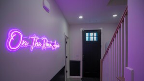 Un couloir orné d’un panneau néon sur lequel on peut lire « On The Road Again » et un escalier avec des rampes en bois.