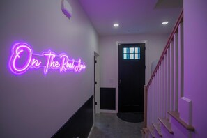 Ein Flur mit einem Neon-Schild, das 'On The Road Again' zeigt, und einer Treppe mit Holellschienen.