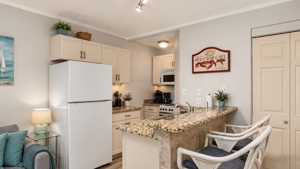 A compact kitchen with a refrigerator, stove, microwave, and a small island with chairs. - SandCastle - Entertainment District - Near Beach (South Padre Island)