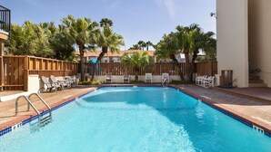 A swimming pool with a wooden deck, lounge chairs, and palm trees. - SandCastle - Entertainment District - Near Beach (South Padre Island)