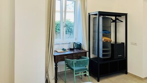 A room with a desk, chair, and a black wardrobe with shelves.