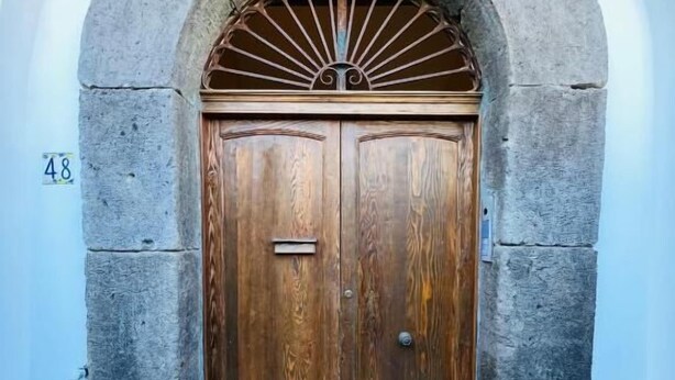 A stone-arched entrance with a wooden double door, a number '48' on the wall, and a small step leading up to the door.