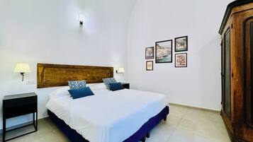 A bedroom with a wooden headboard, a bed with white and blue bedding, two bedside lamps, a nightstand, and a wardrobe.