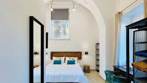 A bedroom with a large bed, a desk, a chair, a bookshelf, and a window with a view of trees.