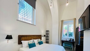 A bedroom with a bed, bedside lamp, window, desk, and a TV.