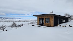 A modern wooden cabin with a large glass door, set in a snowy landscape with a clear sky. - Luxury home with hot tub (Victor)