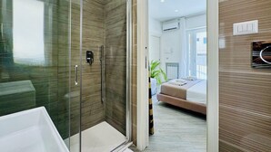 Un baño moderno con cabina de ducha de vidrio, una bañera blanca y un toallero a la vista.
