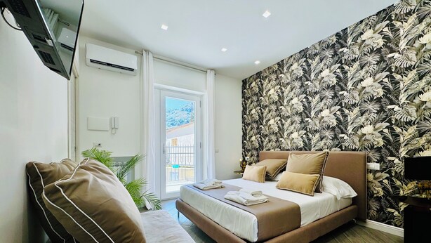 Un dormitorio moderno con cama, sofá, televisión y balcón con vistas.