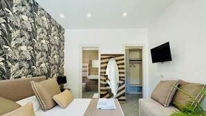 Habitación de hotel con cama, sofá, televisión, baño con espejo y ducha.