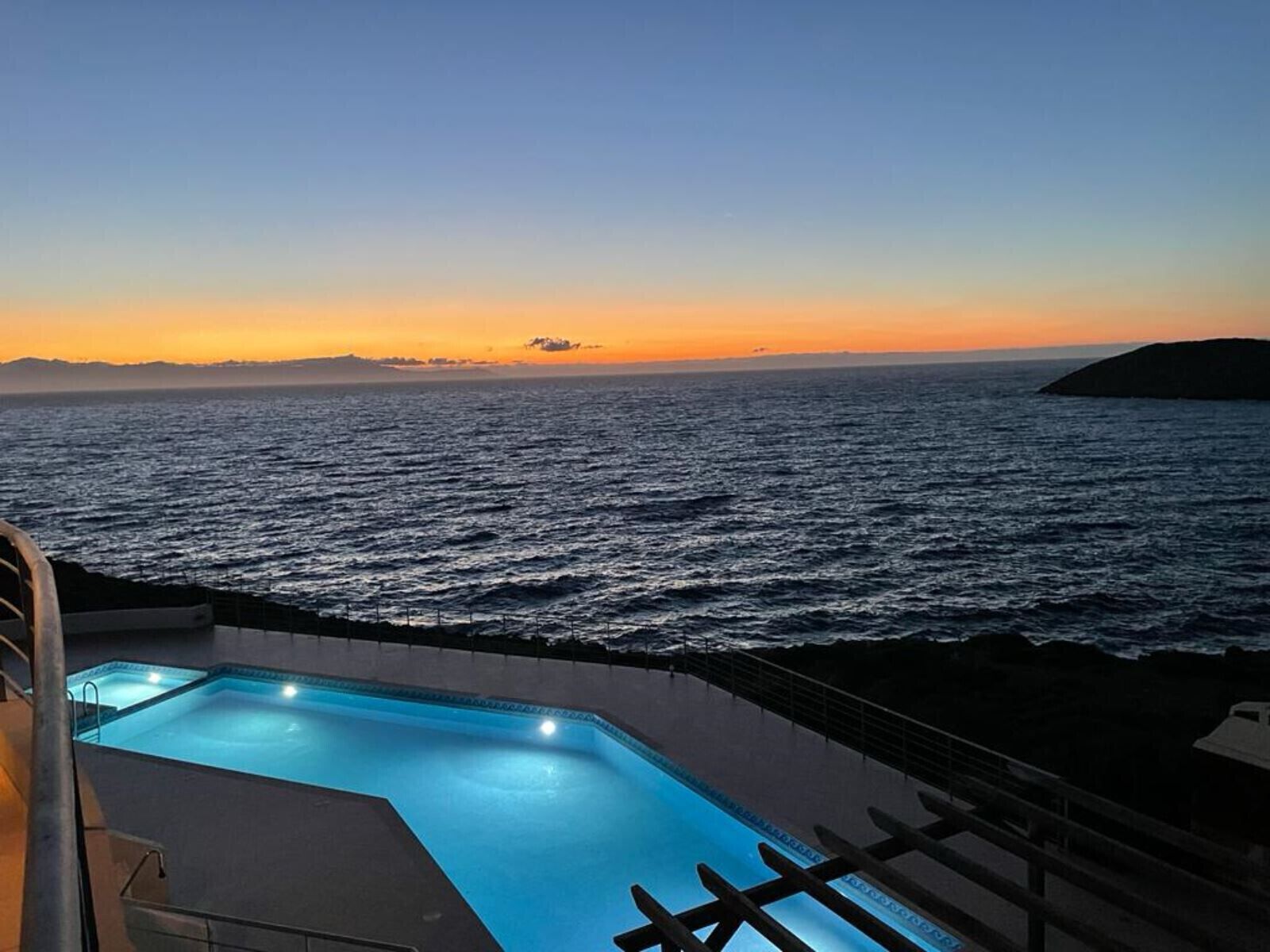 Ein Schwimmbad mit Blick auf das Meer bei Sonnenuntergang.