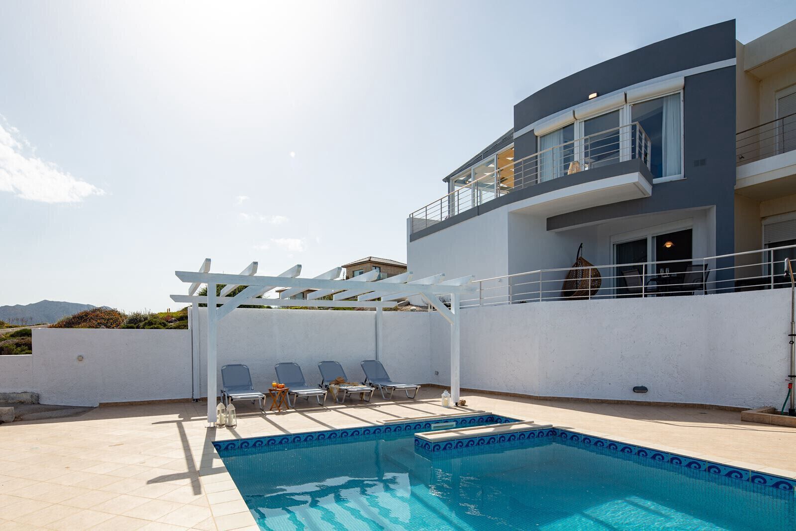 A modern building with a pool, outdoor seating, and a pergola.