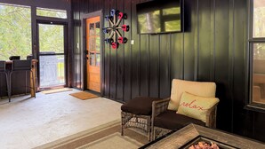 A cozy room with a fireplace, a wicker chair, a cushioned bench, a television, and a door leading outside.