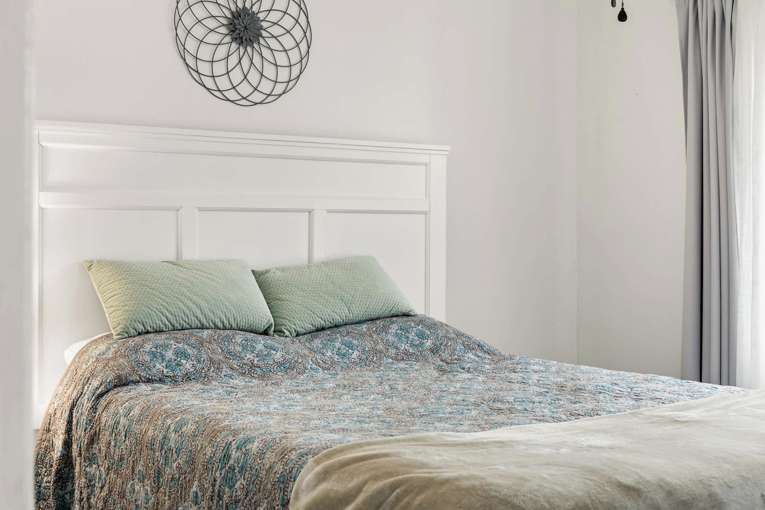 A neatly made bed with a patterned bedspread, a white headboard, and a decorative wall piece above it.