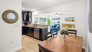 A modern kitchen with dark cabinets, a central island, and a dining area with a wooden table and chairs. - St. Pete Pool Oasis - Steps to the Beach! (Pinellas Park)