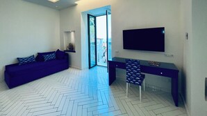 A modern room with a sofa, a desk, a chair, and a TV mounted on the wall. - YourHome - Scirocco Suite (Sorrento)