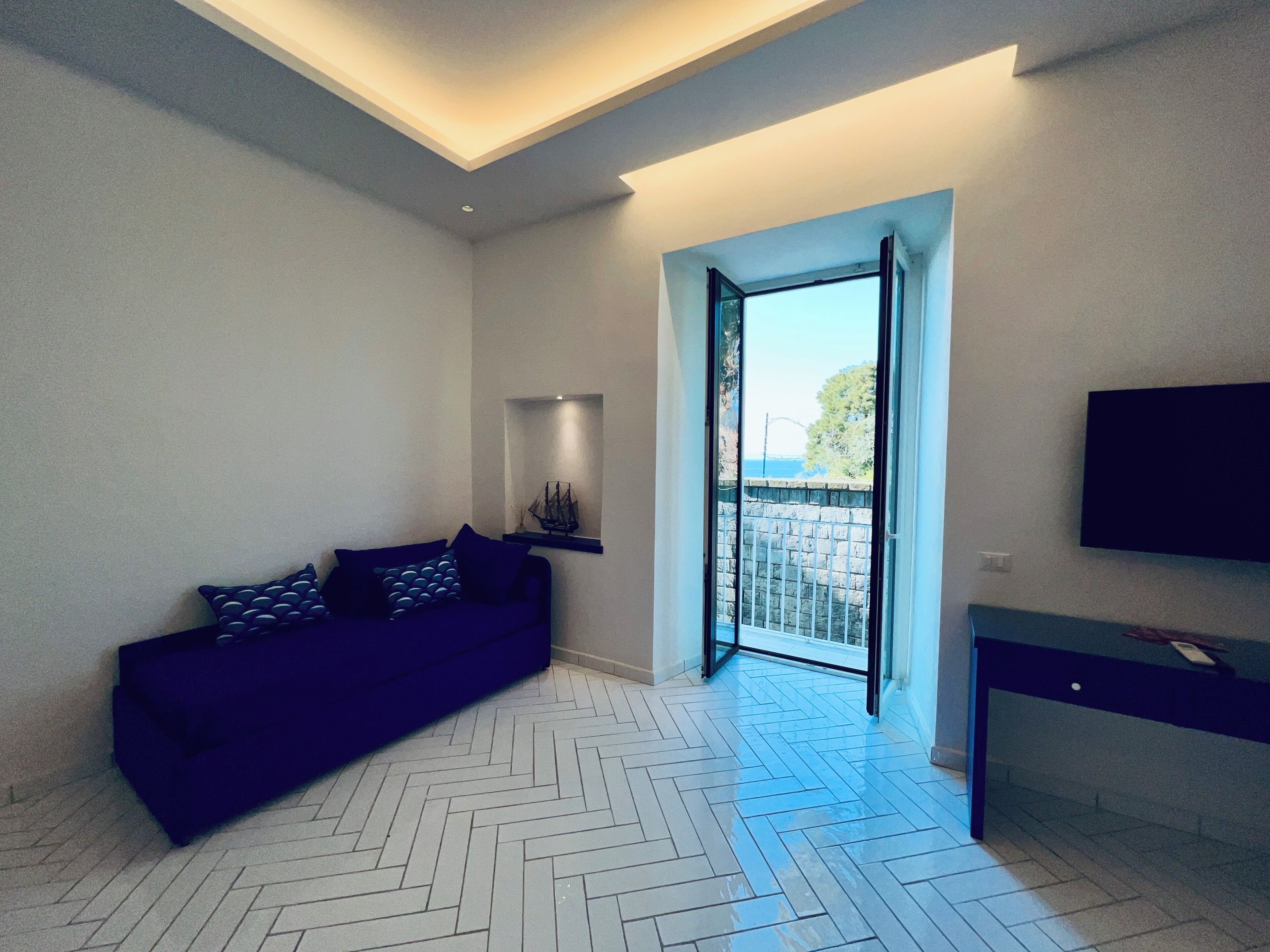 Un moderno salón con suelo de espiga, un sofá azul oscuro, un televisor de pantalla plana en la pared y vistas a través de un ventanal.