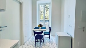 A small kitchen with a dining table, two chairs, a refrigerator, and a window with a view of trees. - YourHome - Scirocco Suite (Sorrento)
