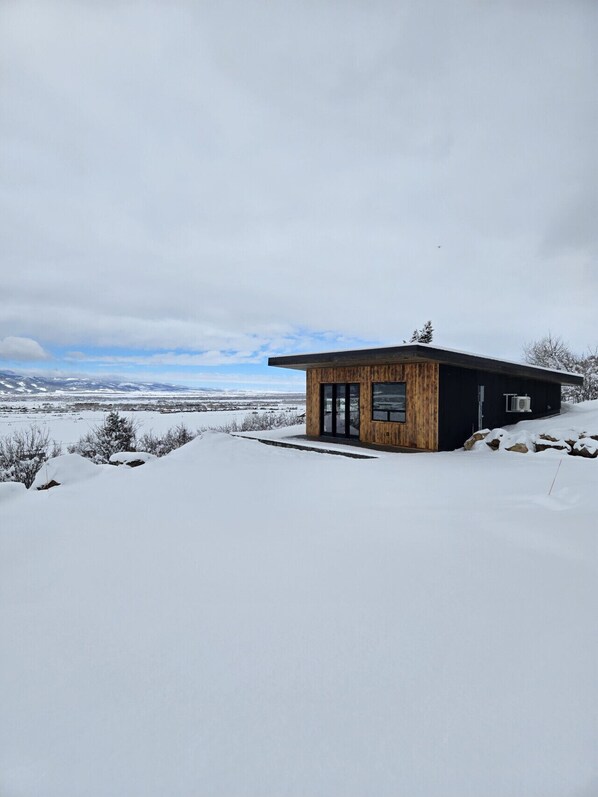 A modern wooden cabin with a large glass door, set in a snowy landscape with a clear sky. - Luxury home with hot tub (Victor)