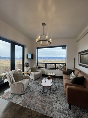 Un ampio soggiorno con una grande finestra che offre vista sul paesaggio, un lampadario moderno e arredamento contemporaneo.