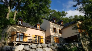 A two-story house with a stone wall, a balcony with chairs, and a wooden deck. - Chalet for 10-12 Guests, 10 min from Peyragudes and Loudenvielle (Cazaux-Fréchet-Anéran-Camors)