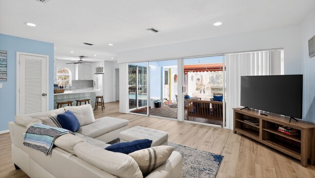 A living room with a sofa, TV stand, and sliding glass doors leading to a patio. - Just Renovated! Waterfront Oasis on the Intracoastal with Pool (Pompano Beach)