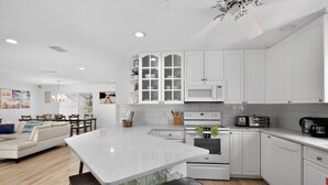 A modern kitchen with white cabinetry, a central island, a dining area with a sofa and table, and a ceiling fan. - Just Renovated! Waterfront Oasis on the Intracoastal with Pool (Pompano Beach)