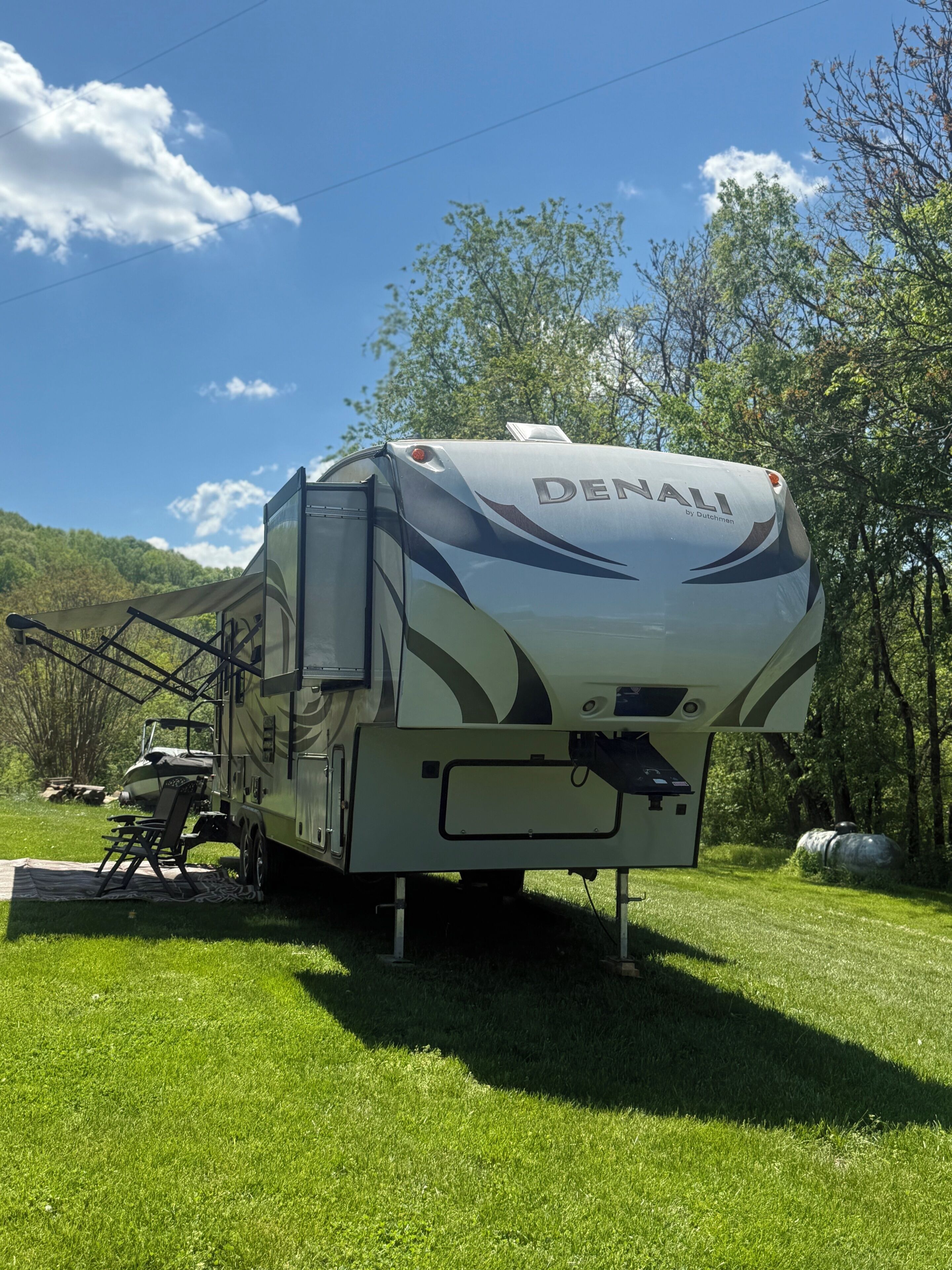 Un camping-car Denauli est stationné sur un champ herbeux, avec des arbres en arrière-plan.