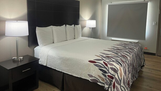 A hotel room with a bed, two bedside lamps, a dark headboard, a window, and a door. - Red Roof Inn Helen, GA - Downtown (Helen)
