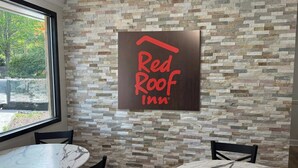 Señal de Red Roof Inn sobre un muro de piedra, dos mesas redondas con sillas y una ventana con vista a árboles.