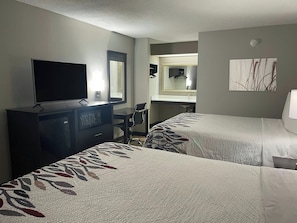 Een hotelkamer met twee bedden, een bureau, een televisie, een spiegel en een badkamer.
