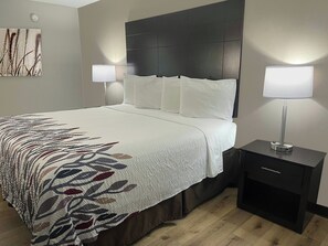 A neatly made bed with white bedding and a patterned throw, a dark headboard, two bedside lamps, and a small bedside table with a lamp. - Red Roof Inn Helen, GA - Downtown (Helen)