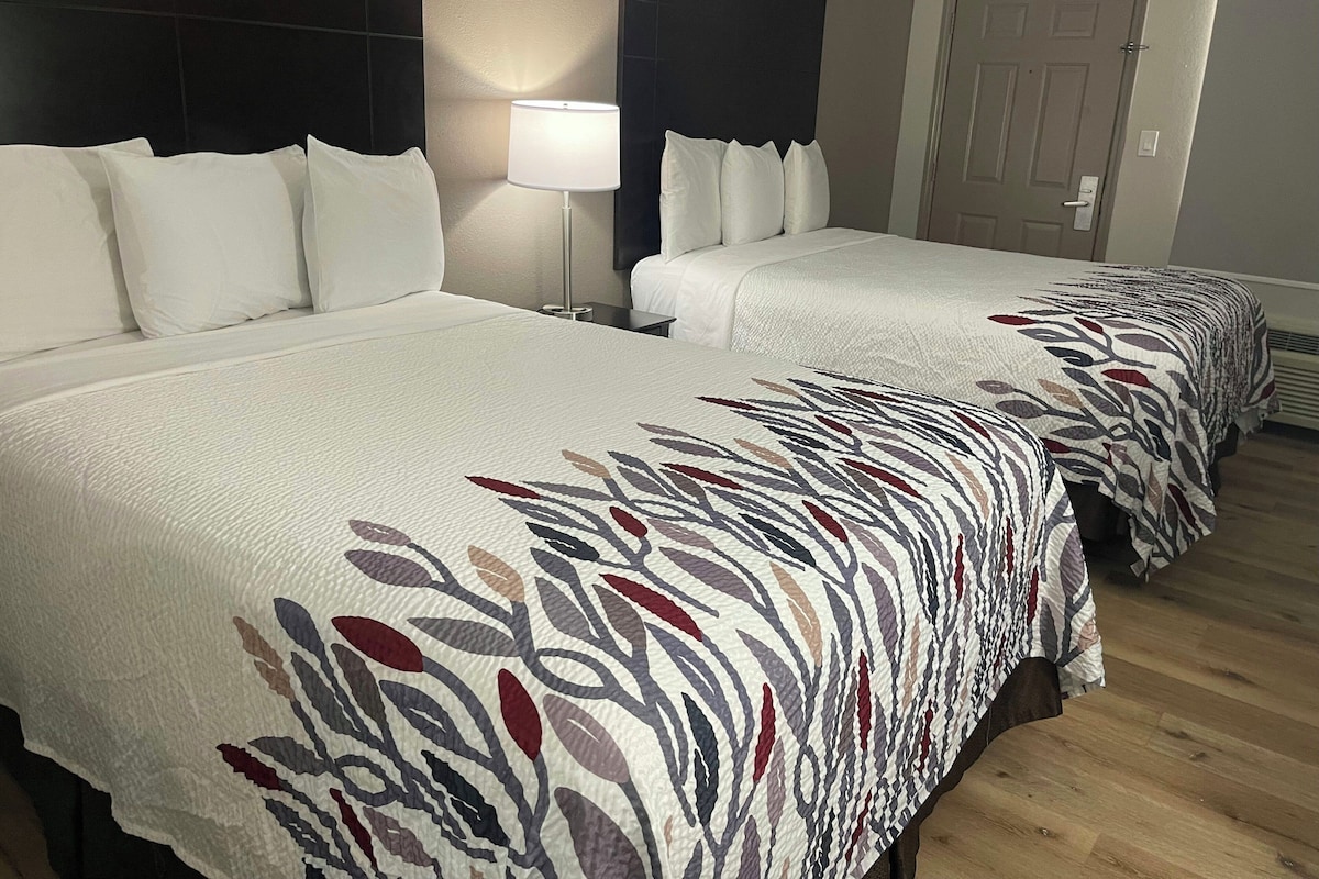 Ein Hotelzimmer mit zwei Betten, einem Nachttisch, einer Lampe und einer Tür.