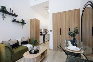 Uma sala de estar moderna com um sofá verde, uma mesa de centro de madeira e um espaço de jantar com uma mesa de vidro posta para dois.