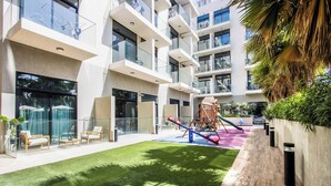 Un bâtiment moderne doté de nombreux balcons, d’une aire de jeux et d’une pelouse bien entretenue.