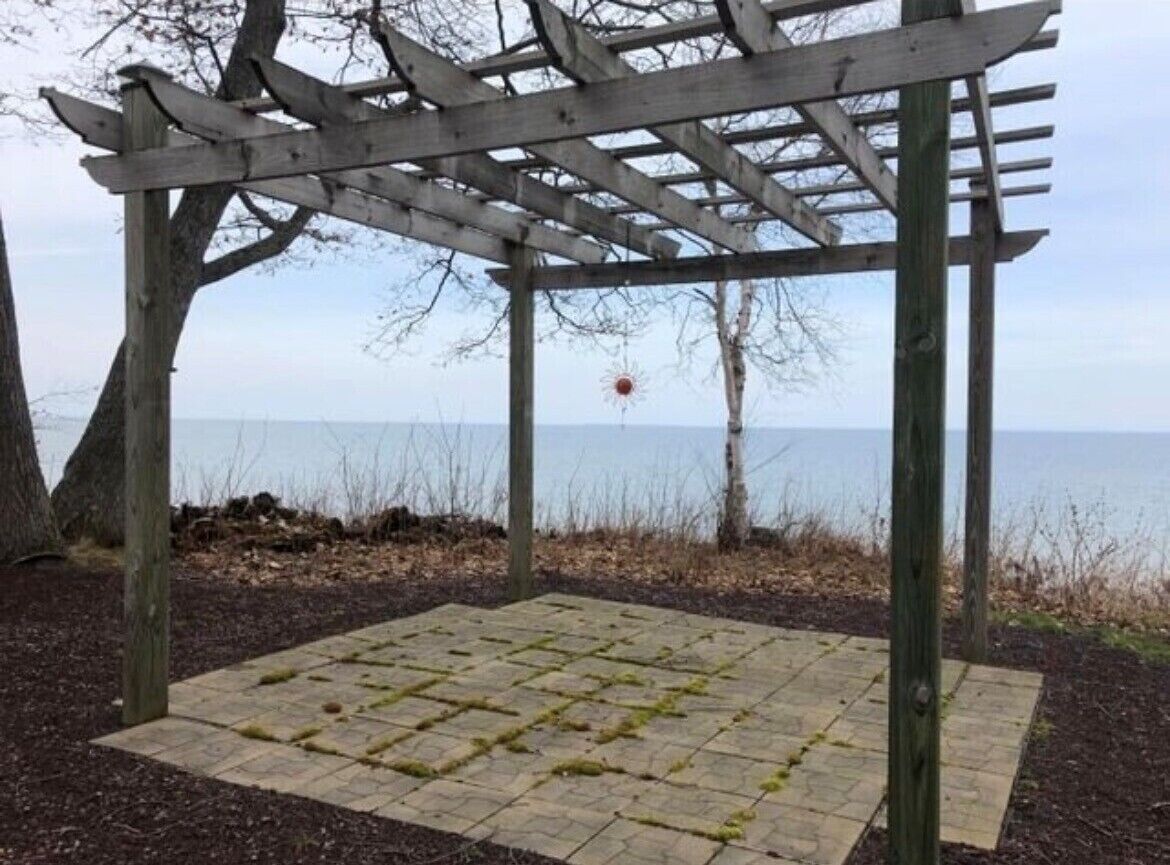Una estructura de pérgola de madera con suelo de baldosas, con vista a un cuerpo de agua.