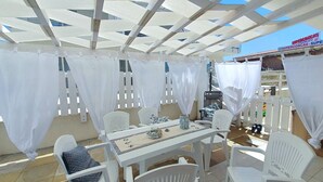 Un patio al aire libre con sillas y una mesa blancos, cubierto por una estructura de toldo blanco.