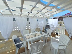 Eine Terrasse im Freien mit weißen Stühlen und einem Tisch, überdacht durch eine weiße Markise.