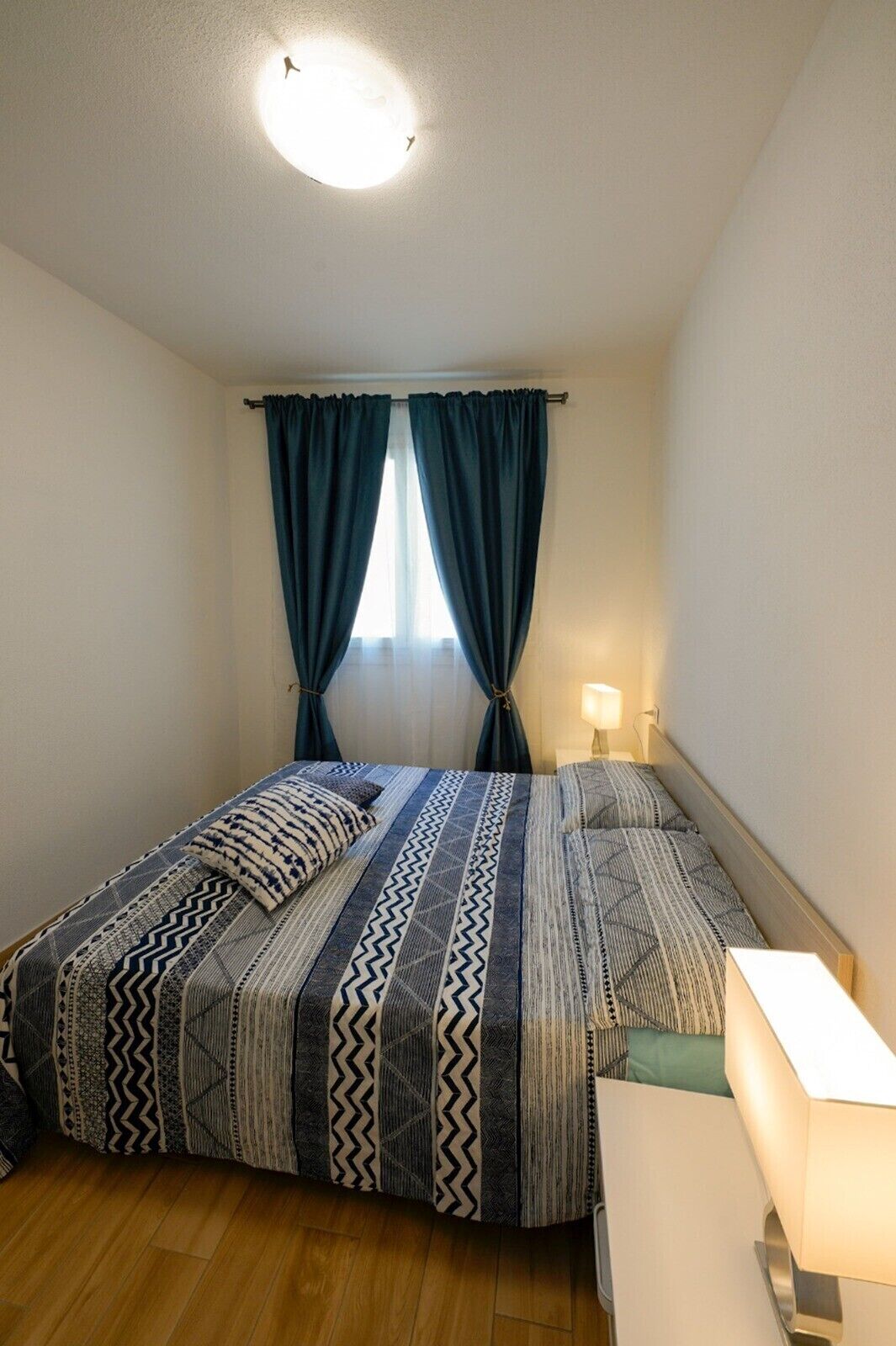 Une chambre à coucher avec un lit, des rideaux, une lampe de chevet et un plancher en bois.