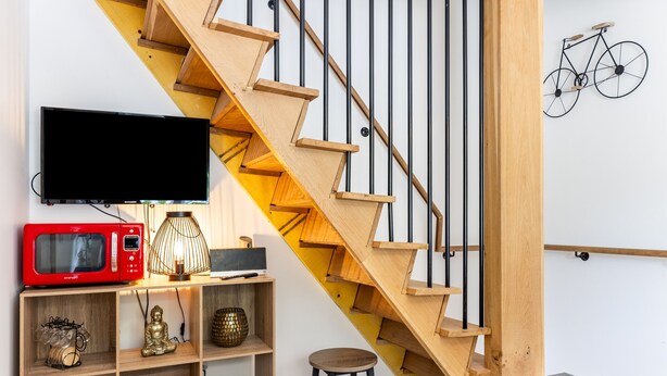Una escalera con escalones de madera y barandillas negras, un televisor montado, un microondas rojo y un estante con objetos decorativos.