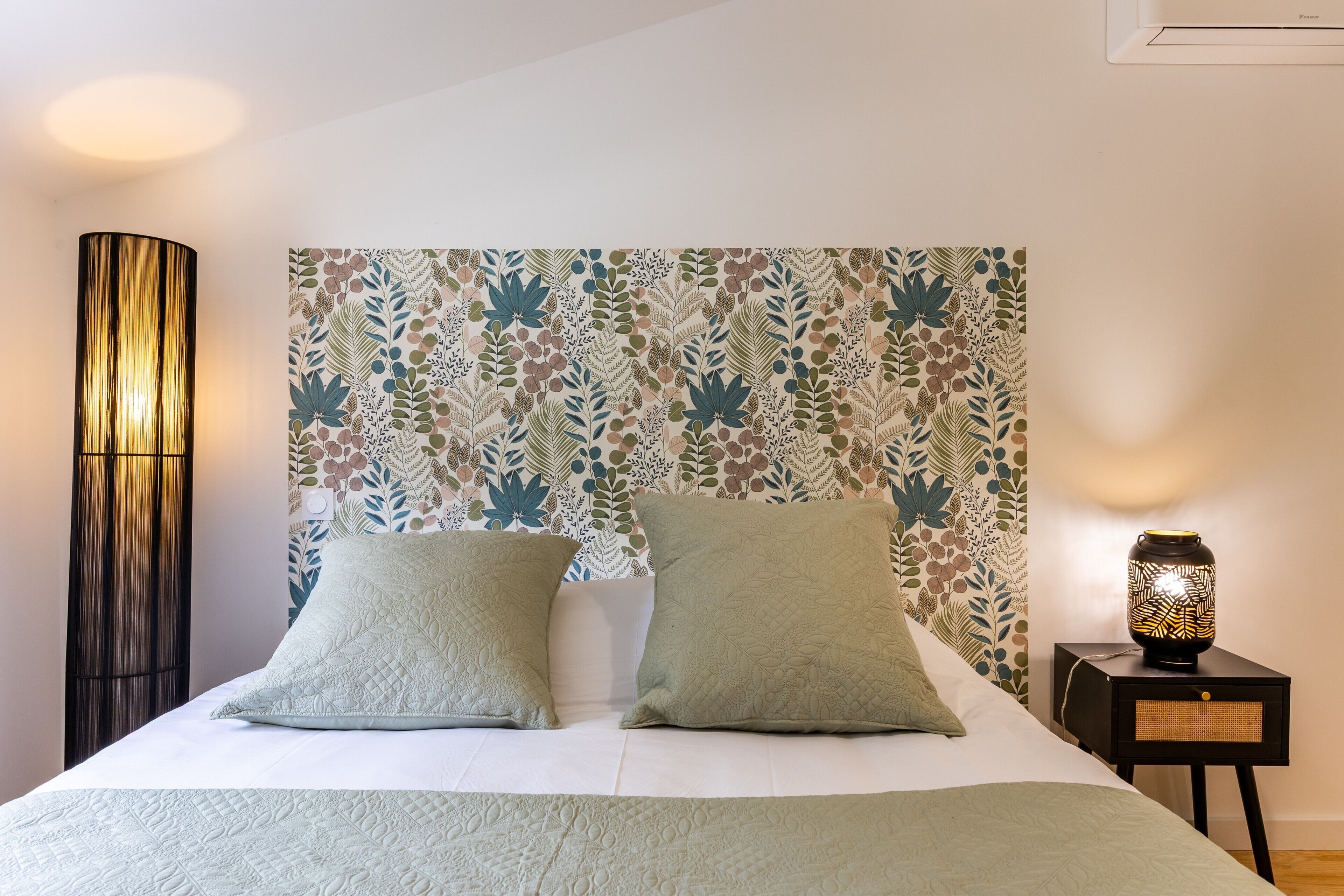 A neatly made bed with two pillows, a bedside lamp, and a patterned headboard.