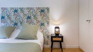 Een slaapkamer met behang met patroon, een bed met groene beddengoed, een nachtkastje met een lamp, en een witte airconditioning.