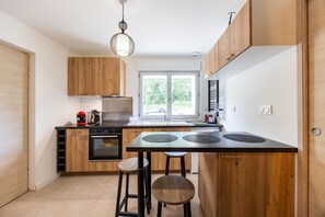 Una cocina moderna con armarios de madera, una isla central, taburetes y una lámpara colgante.
