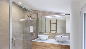 Un baño moderno con ducha de vidrio, dos lavamanos sobre encimera y un mueble de tocador de madera.