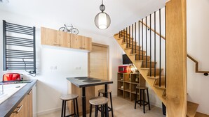 Una cocina compacta con una escalera de madera, una lámpara colgante y una bicicleta en la pared.