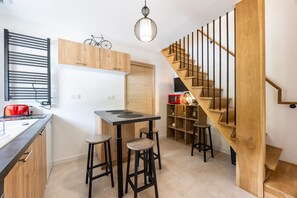 Una cocina compacta con una escalera de madera, una lámpara colgante y una bicicleta en la pared.