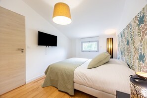 Ein Schlafzimmer mit einem Bett, einem an der Wand montierten Fernseher, einem Fenster und einer Lampe.