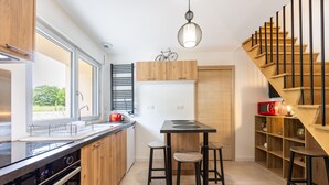 Una cocina moderna con armarios de madera, estufa empotrada, una mesa de comedor con taburetes y una escalera con barandilla de madera.