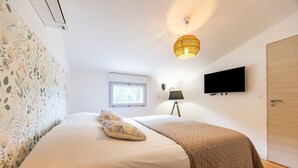 Un dormitorio con cama, ventana, televisión montada en la pared y una puerta.