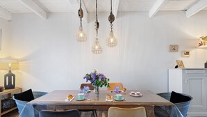 Un'area pranzo con un tavolo in legno, sedie trasparenti, lampade a sospensione e un vaso con fiori.