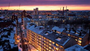 Useita kerroksia käsittävä hotelli, jonka keskellä on sisäpiha, ja jonka ympärillä on lumipeitteisiä rakennuksia, hämärän aikaan.